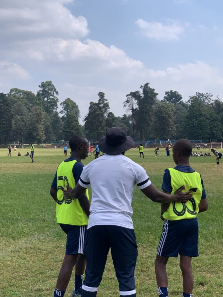 A Kisasa FC coach with an arm around two players on the touchline during a match.