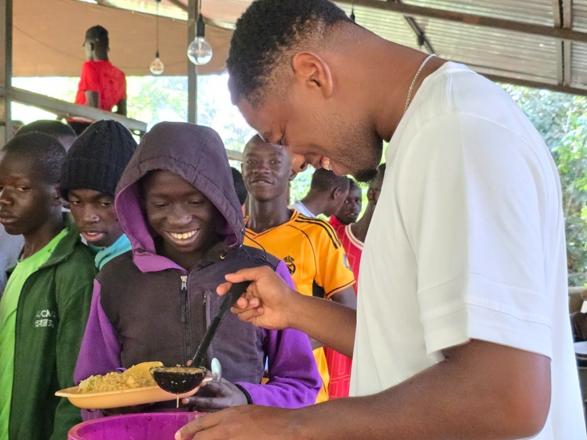 A Kisasa FC coach serves a plate of food to a smiling player in the team meal line.