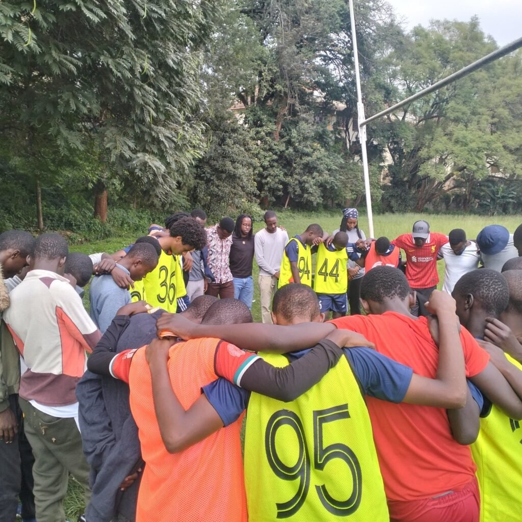 Kisasa FC players, coaches and staff in a linked-arm prayer huddle after training.